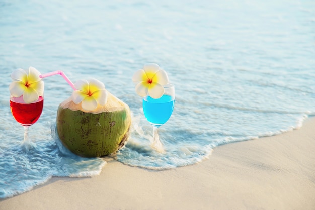 Free photo cocktail glasses with coconut and pineapple on clean sand beach - fruit and drink on sea beach