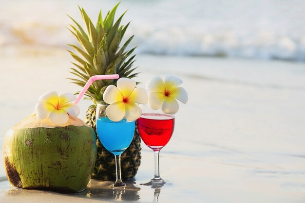 Cocktail glasses with coconut and pineapple on clean sand beach - fruit and drink on sea beach