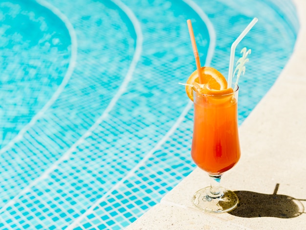 Cocktail with orange slices and straws placed on poolside