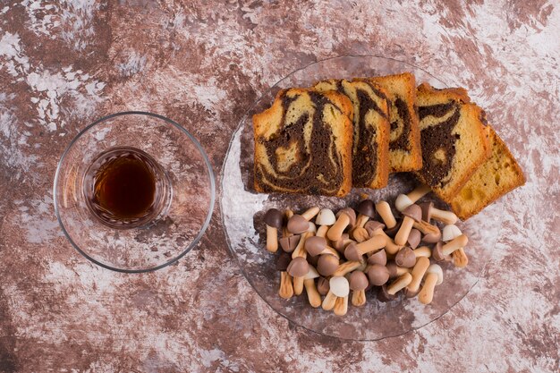 Cocoa cake with waffles and cookies in a glass platter with a glass of tea, top view