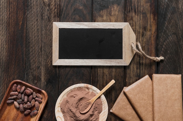 Cocoa powder, beans, wrapped chocolate bar and small wooden slate on wooden table