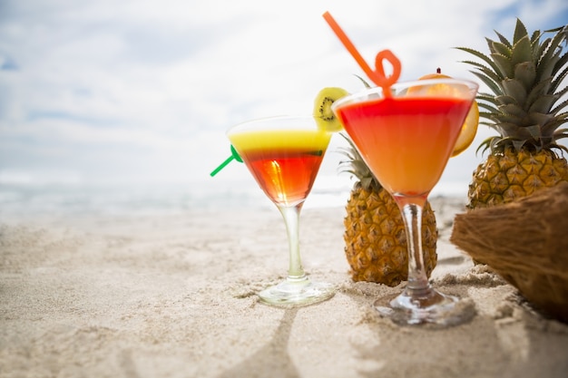 Coconut, pineapple and two glasses of cocktail drink kept on the sand at tropical beach