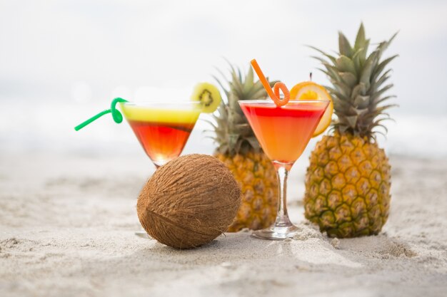 Free Photo coconut, pineapples and two glasses of cocktail drink kept on the sand