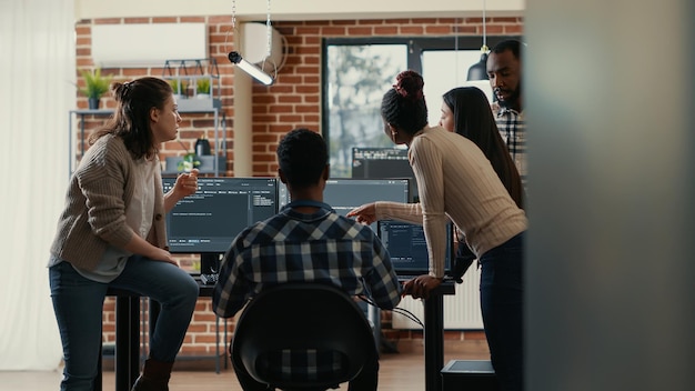 Coders discussing about source code compiling discovers errors and asks the rest of the team for explanations in front of multiple screens running algorithms. Software developers doing teamwork.