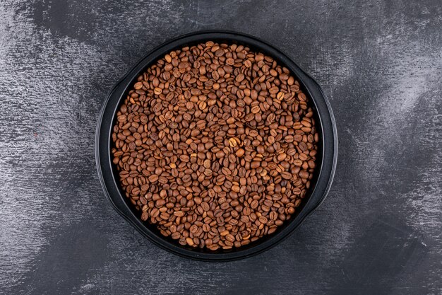 Coffee beans in black pot on dark surface top view