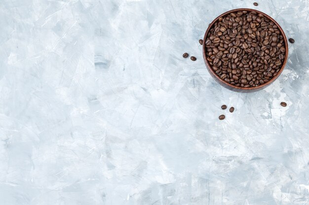 Coffee beans in a clay bowl on a grey plaster background. top view.