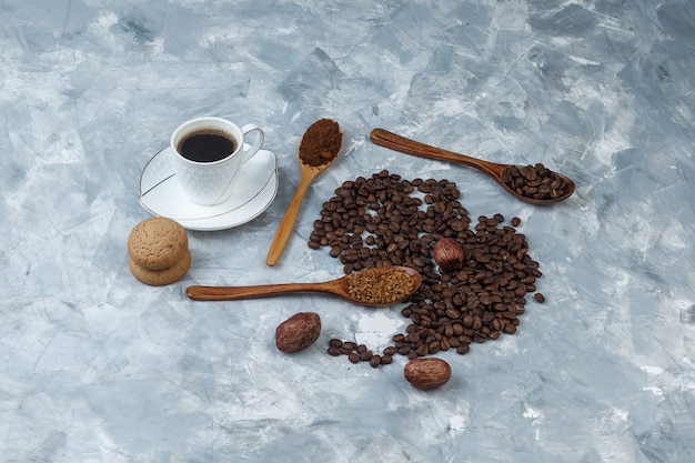 Free photo coffee beans, cup of coffee with instant coffee, coffee flour, coffee beans in wooden spoons, cookies high angle view on a light blue marble background