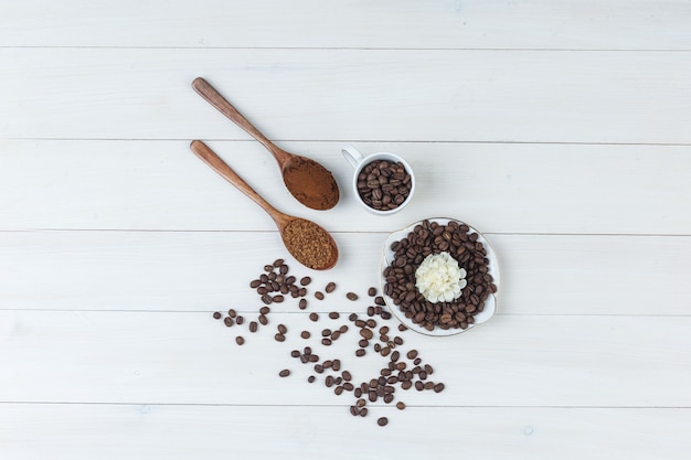 Coffee beans in cup and plate with grinded coffee, flower top view on a wooden background