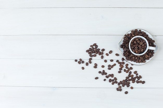 Coffee beans in cup and saucer top view on a wooden background