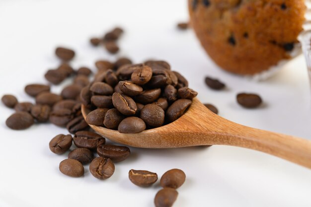 Coffee beans on wooden spoon and Banana Cupcakes on a white wood table.