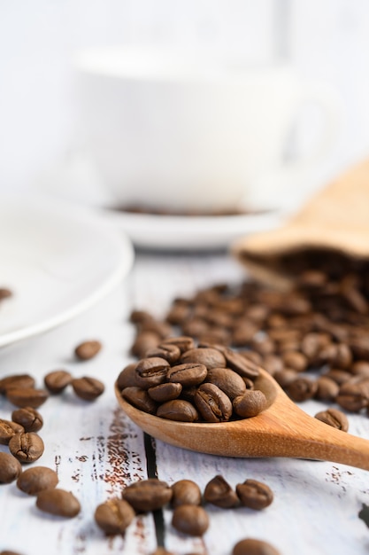 Coffee beans on wooden spoon and hemp sacks on a white wood table.