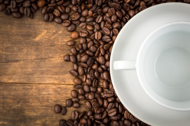 Coffee beans on a wooden table with an empty cup