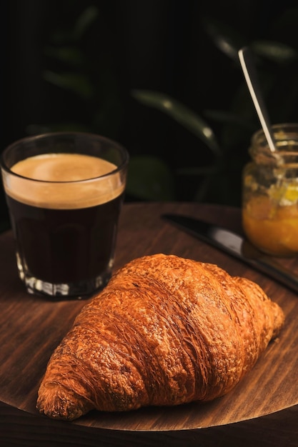 Coffee croissant and jam on a wooden table French breakfast in a cafe Vertical shot selective focus on a croissant