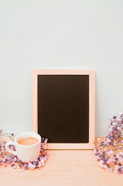 Free photo coffee cup and baby's-breath flowers near the blank wooden slate against white wall