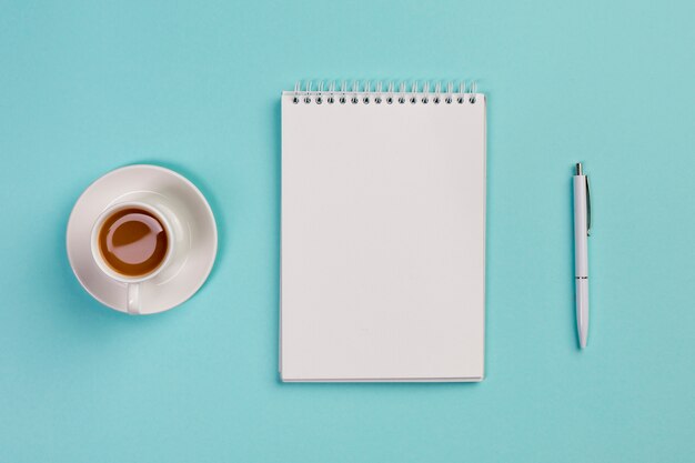 Coffee cup,blank spiral notepad and pen on blue office desk