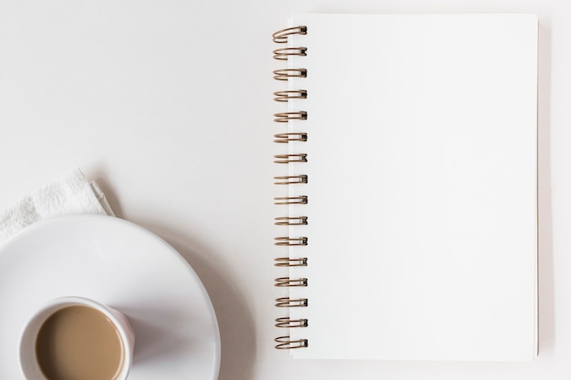 Coffee cup and blank spiral notepad on white background