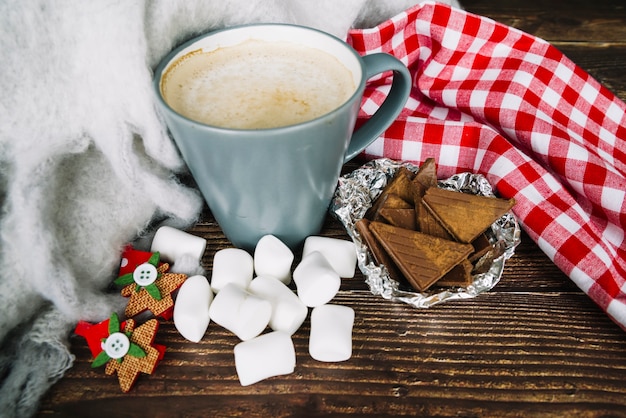 Free photo coffee cup; chocolate pieces and marshmallow on wooden desk in christmas