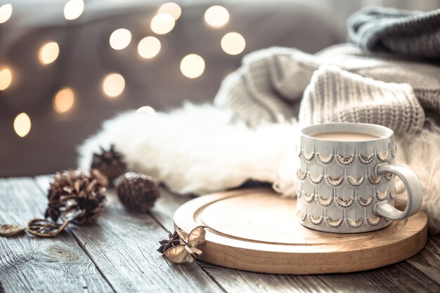 Coffee cup over Christmas lights bokeh in home on wooden table with sweater on a wall and decorations. Holiday decoration