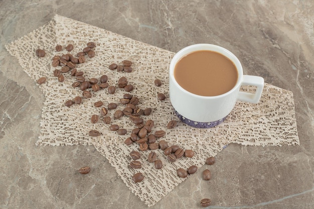 Coffee cup and coffee beans on marble surface with burlap