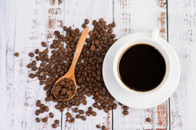 Coffee cup and coffee beans in wooden spoon on white table.