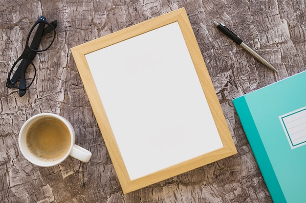 Free photo coffee cup; eyeglasses; picture frame; pen and notebook on textured background