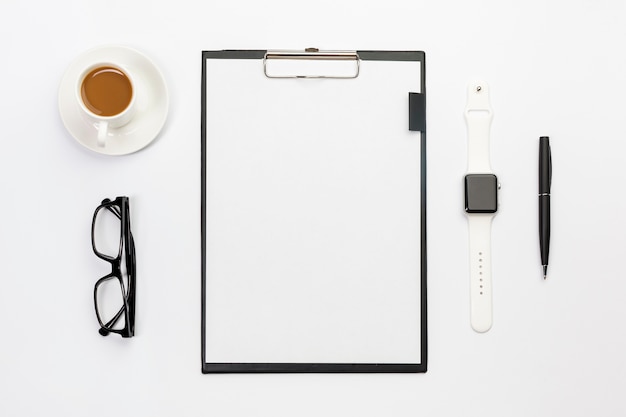 Coffee cup,eyeglasses,smart watch,pen and blank paper clipboard on white desk