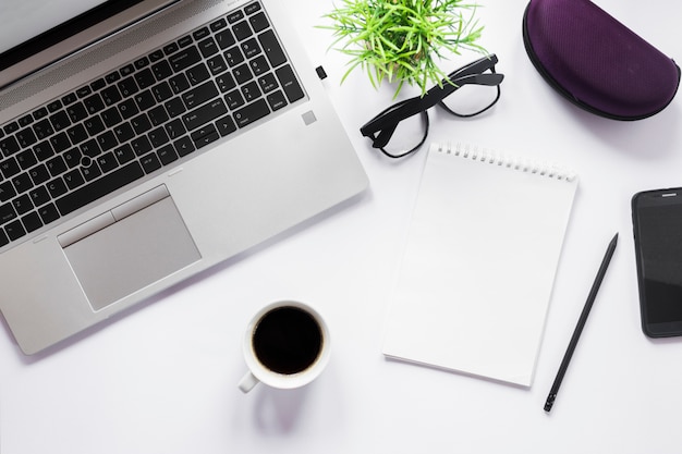 Free photo coffee cup; laptop; eyeglasses; pencil and spiral notepad with pencil on white backdrop