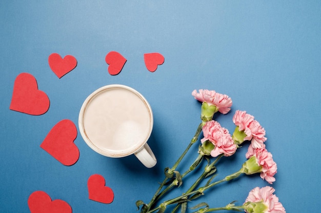 Free photo coffee cup and pink carnation with red heart on blue table top view