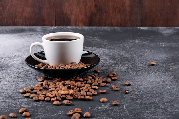 Free Photo coffee cup with coffee beans on dark table