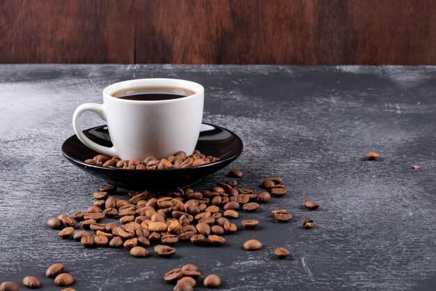 Coffee cup with coffee beans on dark table