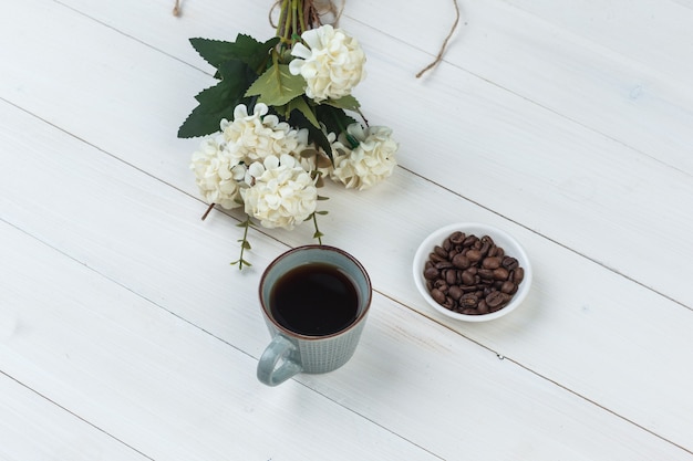 Free photo coffee in a cup with coffee beans, flowers high angle view on a wooden background