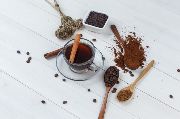 Coffee in a cup with grinded coffee, coffee beans, cinnamon sticks, dried herbs high angle view on a wooden background