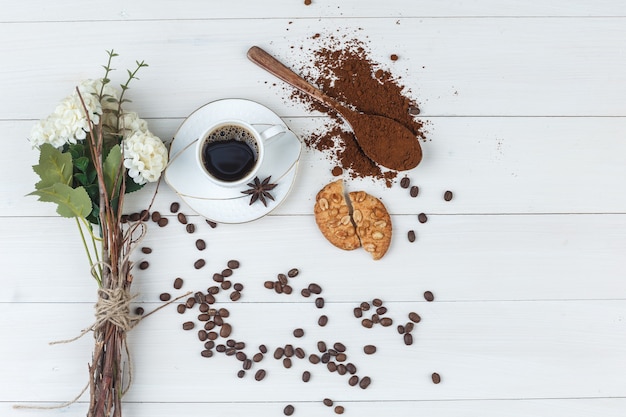 Coffee in a cup with grinded coffee, spices, flowers, coffee beans, cookies flat lay on a wooden background