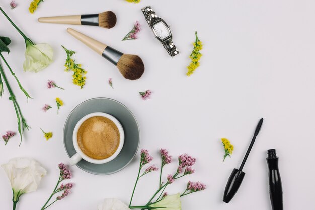 Coffee cup; wristwatch; makeup brush; mascara bottle with fresh flowers on white background