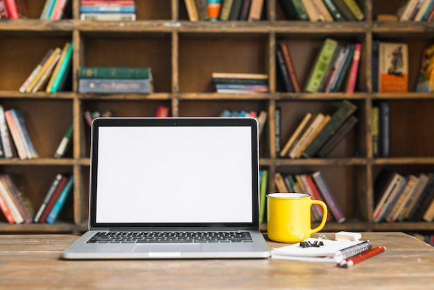 Coffee mug and laptop with stationeries on wooden desk in library