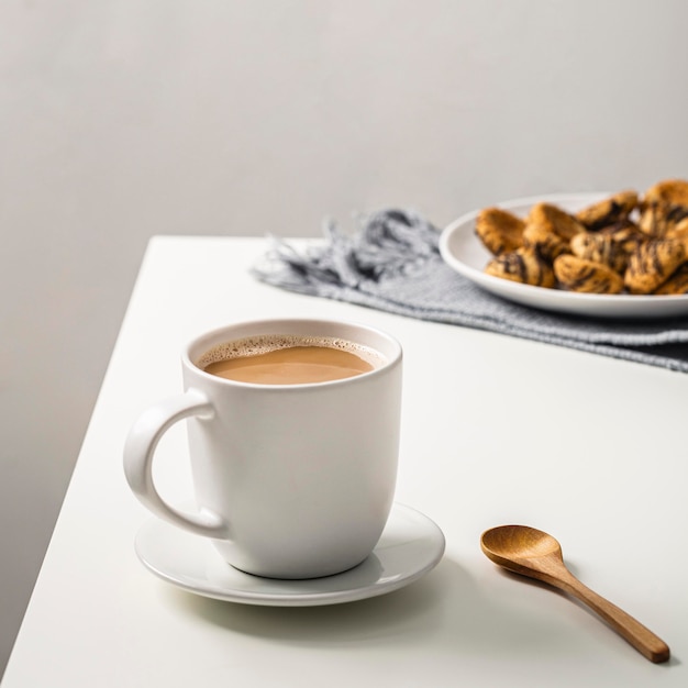 Coffee mug on table with cookies on plate and spoon