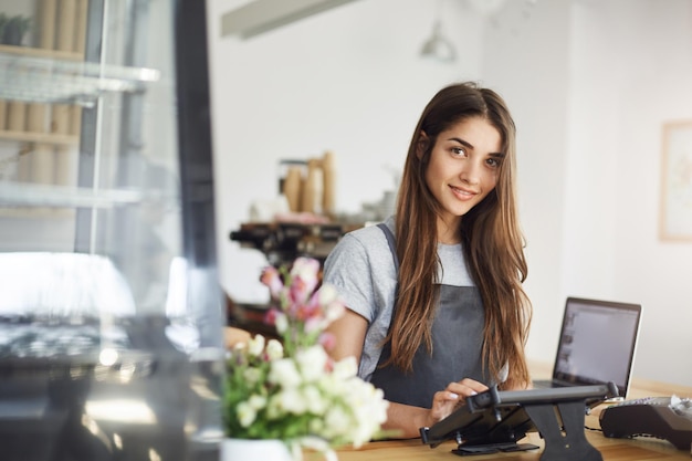 Coffee shop owner using a tablet looking at camera smiling waiting for her first customer