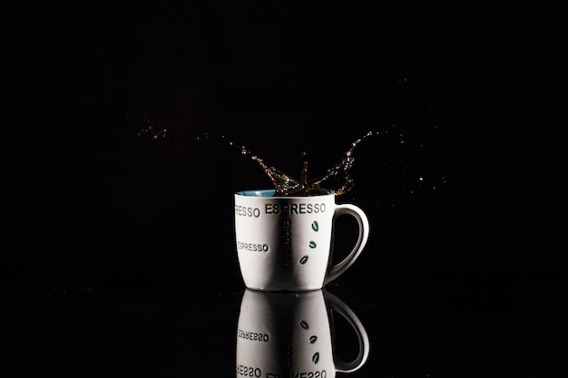 Coffee splashes in white cup on black background