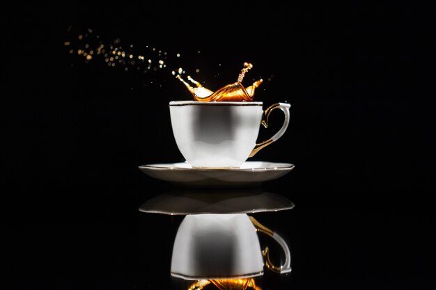 Coffee splashes in white cup on black background