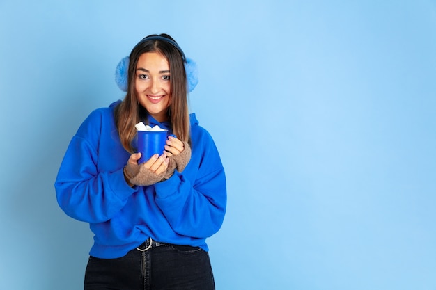 Free photo coffee time. caucasian woman's portrait on blue  space. beautiful female model in warm clothes