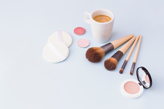 Free photo coffee with makeup brush; eyeshadow; sponge and blusher on white background