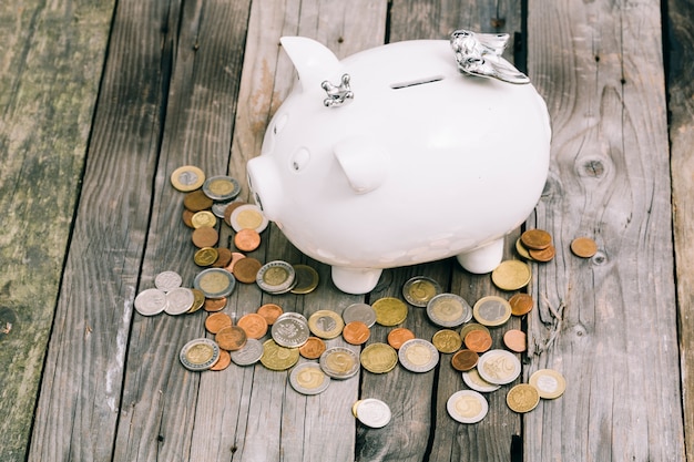 Coins around the white piggy bank on an old wooden table