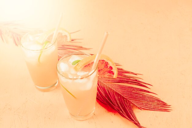 Cold grapefruit and orange cocktail in two glasses with ice cubes on colored background