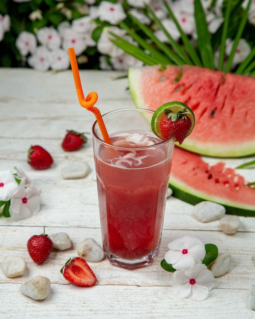 Cold watermelon strawberry kuice with ice cubes and fruits around.