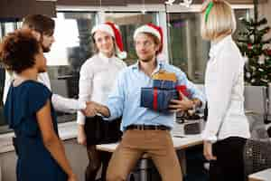 Free photo colleagues celebrating christmas party in office smiling giving presents.