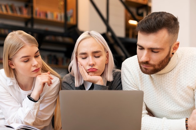 Colleagues talking and studying in a library using a laptop