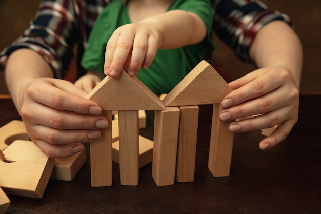 Free Photo collecting wooden constructor like house. close up shot of female and kid's hands doing different things together. family, home, education, childhood, charity concept. mother and son or daughter.