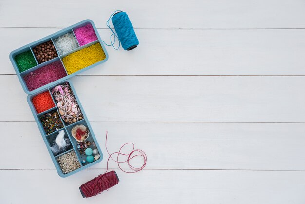 Collection of beads in blue case with bright blue and purple yarn spool on white desk