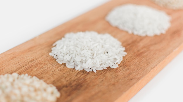 Collection of uncooked rice on wooden tray