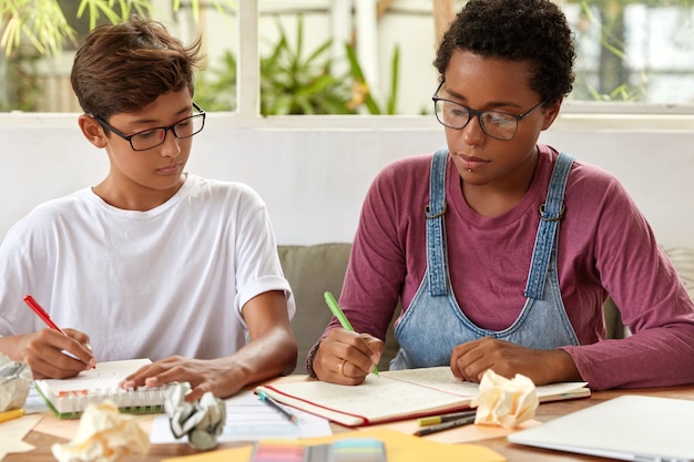 College students focused on writing, sit at desktop, make notes in notebook